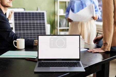 Téléchargez les photos : Gros plan de l'ordinateur portable avec écran vide sur la table avec des gens d'affaires travaillant en arrière-plan - en image libre de droit