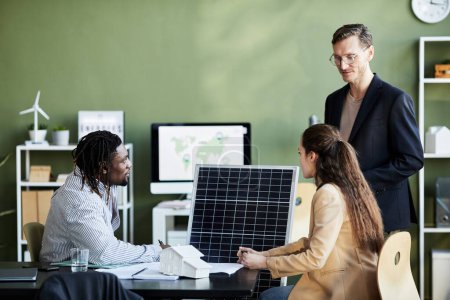 Foto de Grupo de empresarios que desarrollan paneles solares para energía alternativa mientras se sientan a la mesa en la reunión en la oficina - Imagen libre de derechos