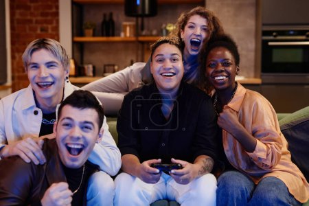 Téléchargez les photos : Groupe de jeunes amis excités interculturels assis devant le téléviseur et jouer au jeu vidéo ensemble tandis que la femme noire en utilisant joystick - en image libre de droit