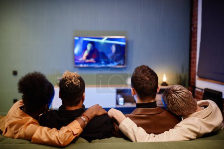 Téléchargez les photos : Vue arrière de deux jeunes couples homosexuels affectueux regardant un film assis sur le canapé devant le téléviseur à loisir ou le week-end - en image libre de droit