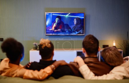 Téléchargez les photos : Écran de télévision sur le mur avec photo de deux jeunes musiciens masculins travaillant en studio et quatre amis regardant un film dans le salon - en image libre de droit