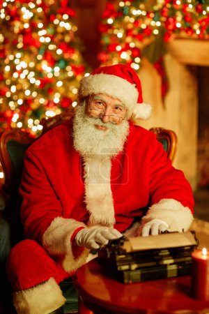 Foto de Retrato vertical de Papá Noel tradicional mirando a la cámara y sonriendo en la habitación festiva con decoraciones navideñas - Imagen libre de derechos