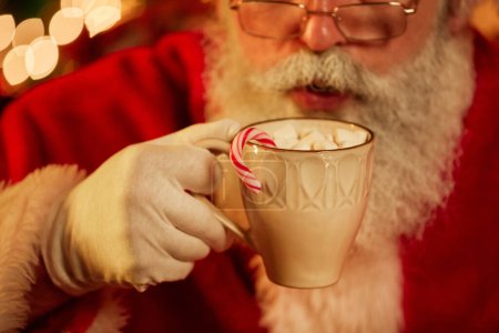 Photo for Close up of traditional Santa Claus enjoying cup of hot chocolate with marshmallows and Christmas sugar cane, copy space - Royalty Free Image