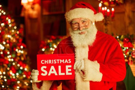Photo for Waist up portrait of traditional Santa Claus holding red SALE sign while standing in decorated room on Christmas - Royalty Free Image