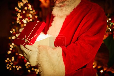 Photo for Side view closeup of traditional Santa Claus opening gift box with magic light inside, copy space - Royalty Free Image