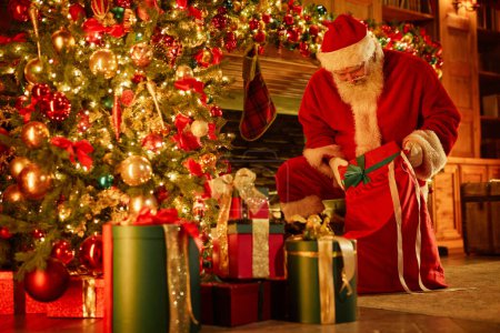 Foto de Retrato de longitud completa de Papá Noel tradicional poniendo regalos bajo el árbol de Navidad, espacio para copiar - Imagen libre de derechos
