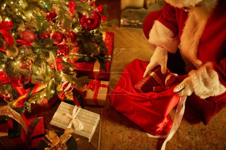 Photo for High angle closeup of traditional Santa Claus putting presents under Christmas tree, copy space - Royalty Free Image