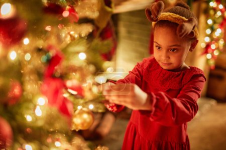 Foto de Retrato mágico de una linda niña decorando el árbol de Navidad con luces centelleantes, espacio para copiar - Imagen libre de derechos