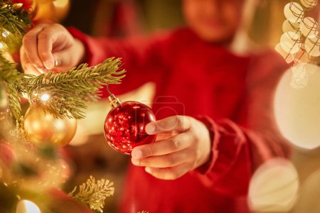 Foto de Primer plano de niña irreconocible decorando el árbol de Navidad con adornos y luces centelleantes, espacio para copiar - Imagen libre de derechos