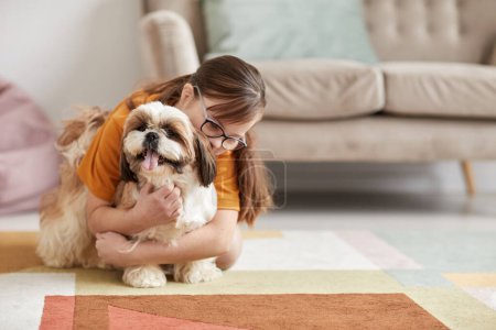 Photo for Minimal full length portrait of teenage girl with Down syndrome playing with dog on floor in cozy home interior, copy space - Royalty Free Image