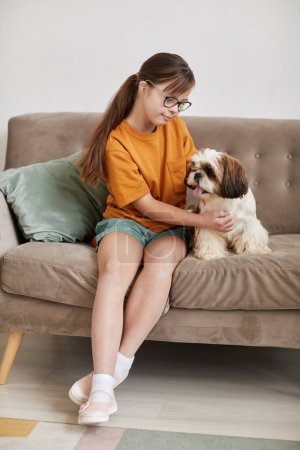 Photo for Full length portrait of teenage girl with Down syndrome playing with small dog while sitting on couch together - Royalty Free Image