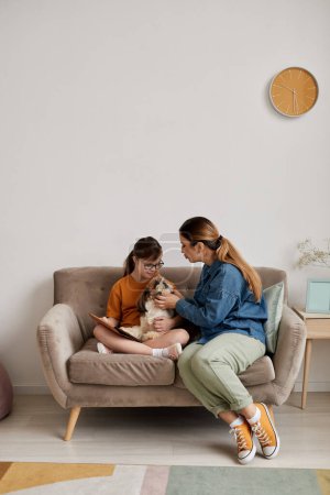 Minimal portrait pleine longueur de mère et fille avec trisomie 21 jouer avec le chien assis sur le canapé à la maison