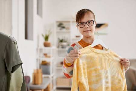 Photo for Waist up portrait of teenage girl with Down syndrome choosing clothes and looking at camera, copy space - Royalty Free Image