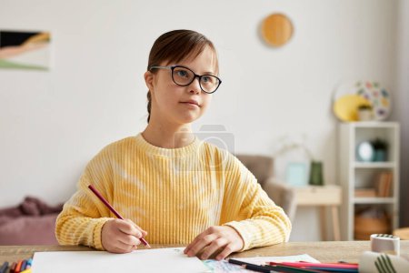 Photo for Minimal portrait of teenage girl with Down syndrome drawing pictures at table and looking away - Royalty Free Image