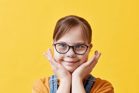 Foto de Primer plano retrato de linda chica con síndrome de Down mirando a la cámara contra el fondo amarillo en el estudio - Imagen libre de derechos
