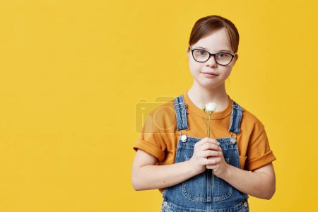 Photo for Waist up portrait of teen girl with Down syndrome looking at camera against yellow background in studio - Royalty Free Image