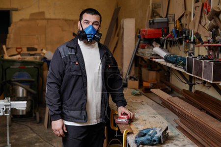 Photo for Waist up portrait of man wearing respirator in workshop and looking at camera, copy space - Royalty Free Image