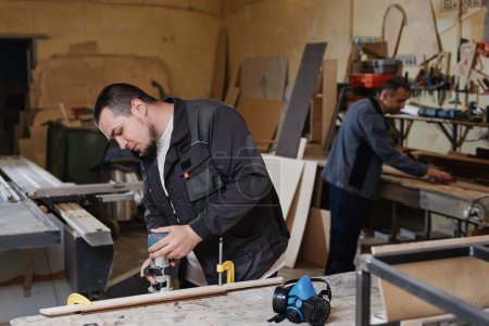 Téléchargez les photos : Portrait latéral d'un ouvrier découpant du bois avec outil électrique dans un atelier d'usine, espace de copie - en image libre de droit