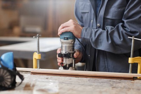Téléchargez les photos : Gros plan d'un ouvrier masculin méconnaissable coupant du bois avec un outil électrique dans un atelier d'usine, espace de copie - en image libre de droit