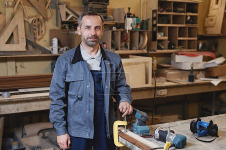 Téléchargez les photos : Portrait taille haute d'un travailleur souriant regardant la caméra debout dans un atelier d'usine, espace de copie - en image libre de droit