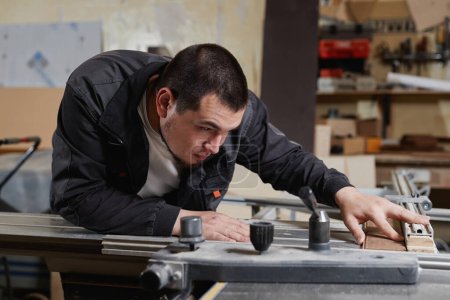 Téléchargez les photos : Portrait latéral d'un ouvrier utilisant une machine à couper le bois en atelier et mesurant soigneusement - en image libre de droit