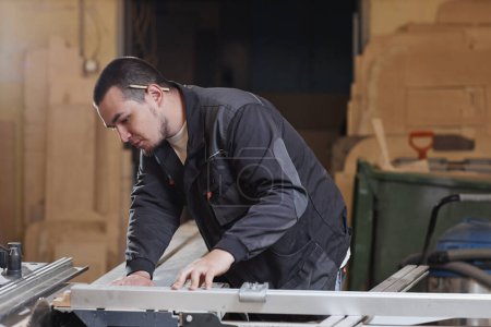 Foto de Retrato de vista lateral de un joven trabajador masculino utilizando una máquina de corte de madera en el taller - Imagen libre de derechos