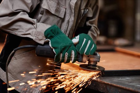 Foto de Primer plano de un trabajador masculino irreconocible cortando metal con herramienta eléctrica en el taller, chispas volando, espacio para copiar - Imagen libre de derechos