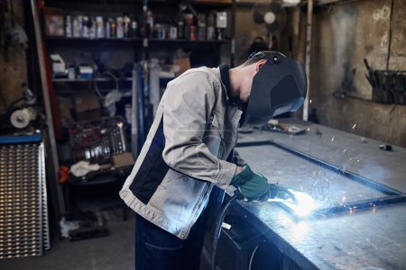 Foto de Retrato de vista lateral de metal de soldadura de trabajador masculino en taller de fábrica industrial con foco en chispas, espacio de copia - Imagen libre de derechos