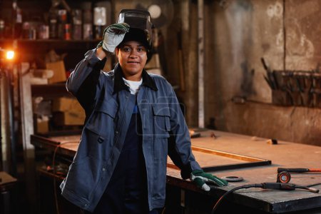 Foto de Retrato de cintura hacia arriba del soldador femenino multiétnico sonriendo a la cámara en el taller de fábrica industrial - Imagen libre de derechos