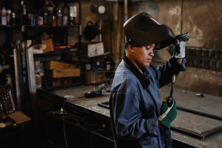 Foto de Retrato de vista lateral de mujer soldadora inspeccionando herramientas en taller industrial, espacio de copia - Imagen libre de derechos
