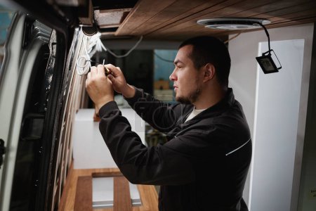 Photo for Side view portrait of man building camper van and installing wires for electrics - Royalty Free Image