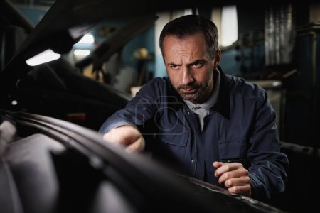 Photo for Portrait of mature car mechanic repairing engine in shop with intense face expression - Royalty Free Image