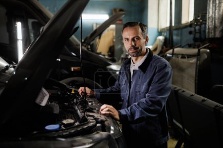 Photo for Waist up portrait of mature car mechanic repairing trucks in garage and looking at camera with accent light, copy space - Royalty Free Image