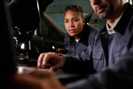 Photo for Portrait of female mechanic using laptop during car checkup in garage with accent light - Royalty Free Image