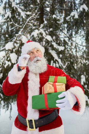 Photo for Vertical portrait of traditional Santa Claus holding presents in winter forest and looking up - Royalty Free Image