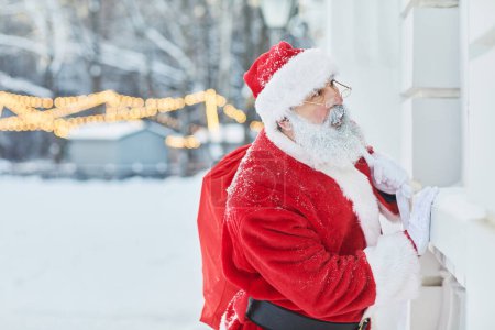 Foto de Retrato de vista lateral de Santa Claus tradicional mirando en las ventanas en la víspera de Navidad, espacio para copiar - Imagen libre de derechos