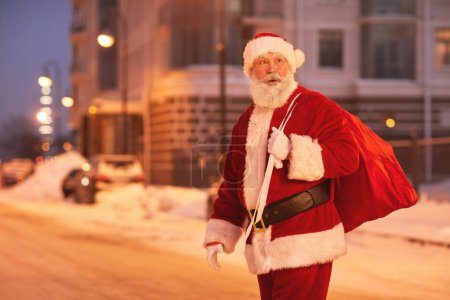 Foto de Retrato de Santa Claus caminando por la ciudad por la noche y mirando a su alrededor, espacio para copiar - Imagen libre de derechos