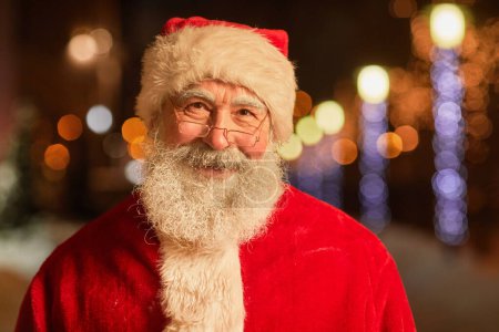 Foto de Retrato del tipo Santa Claus mirando a la cámara y sonriendo en el entorno nocturno de la ciudad - Imagen libre de derechos