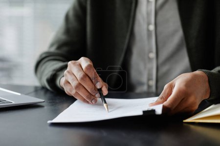 Foto de Primer plano del hombre negro anónimo leyendo contrato en la reunión y firmándolo con pluma, espacio de copia - Imagen libre de derechos