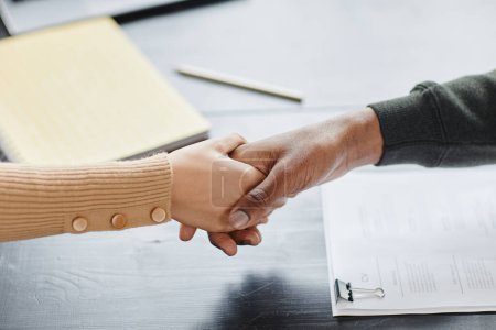 Photo for High angle closeup of two people shaking hands over meeting table in office after successful deal or job interview - Royalty Free Image