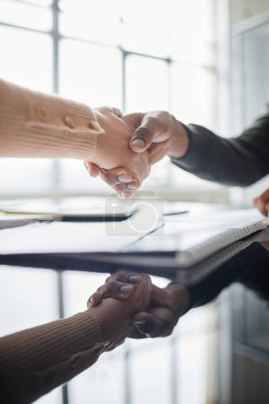 Foto de Primer plano vertical de dos personas estrechando las manos sobre la mesa de reunión en la oficina con reflejo de espejo - Imagen libre de derechos