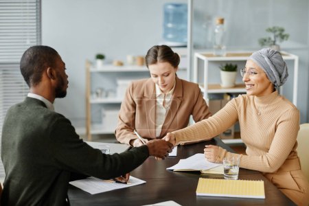 Photo for Diverse group of people in meeting or job interview at office setting, focus on Middle Eastern woman shaking hands with candidate - Royalty Free Image