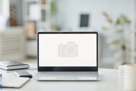 Téléchargez les photos : Image de fond de l'ordinateur portable ouvert avec maquette d'écran blanc sur le lieu de travail dans des tons intérieurs de bureau minimes blanc et gris, espace de copie - en image libre de droit