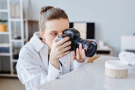 Téléchargez les photos : Vue de côté portrait de jeune femme prenant des images de produits de crème de beauté à la main avec caméra professionnelle - en image libre de droit