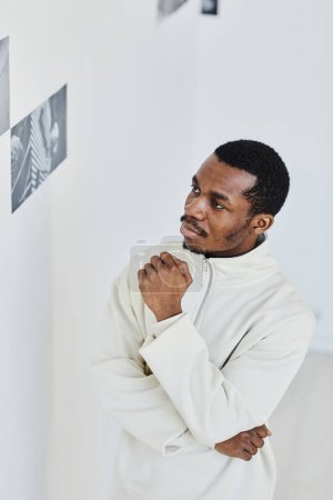 Foto de Mínimo retrato de hombre negro guapo mirando imágenes en la galería de fotos y disfrutando del arte - Imagen libre de derechos