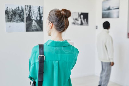 Photo for Back view of young woman wearing green while looking at art in gallery or museum, copy space - Royalty Free Image