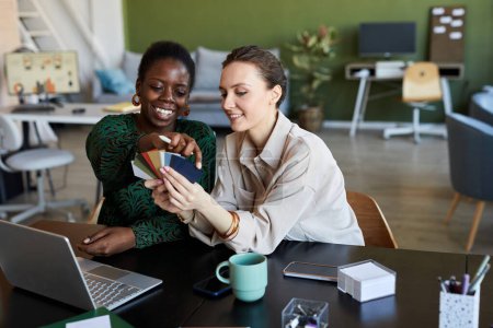 Téléchargez les photos : Deux jeunes femmes d'affaires interculturelles choisissant la couleur de la palette tout en travaillant sur la création de nouveaux produits à la réunion - en image libre de droit