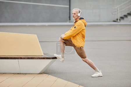 Foto de Retrato mínimo de hombre maduro deportivo que se extiende al aire libre con auriculares en el entorno urbano de la ciudad, espacio de copia - Imagen libre de derechos