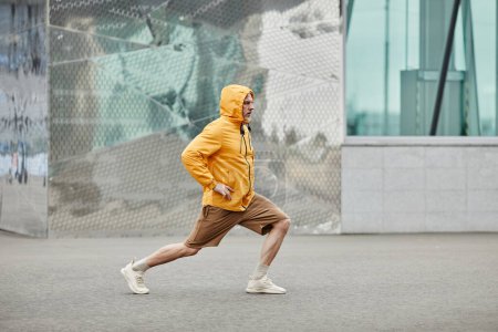 Photo for Minimal side view portrait of sportive mature man stretching outdoors in urban city setting and wearing contrasted yellow jacket - Royalty Free Image