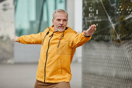 Foto de Retrato de la cintura hacia arriba del hombre maduro guapo haciendo ejercicios al aire libre en la ciudad urbana, usando chaqueta amarilla, espacio para copiar - Imagen libre de derechos